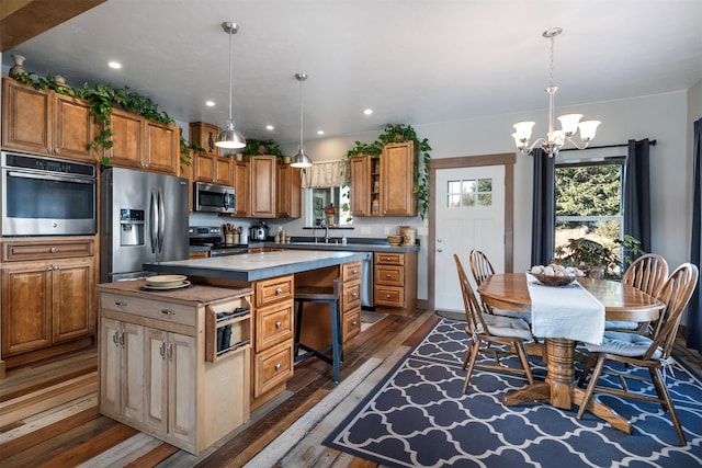 kitchen featuring appliances with stainless steel finishes, dark wood-style flooring, a chandelier, a sink, and a kitchen island