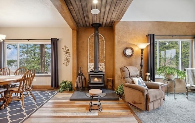 living area with a wood stove, healthy amount of natural light, wood finished floors, wood ceiling, and baseboards