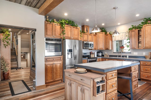 kitchen featuring appliances with stainless steel finishes, wood finished floors, a sink, a kitchen island, and hanging light fixtures