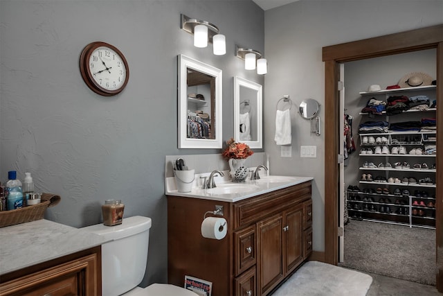 bathroom featuring a walk in closet, toilet, and a sink