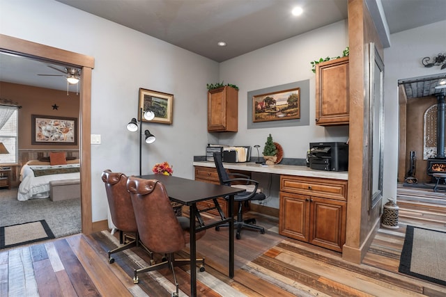 office area with a wood stove, recessed lighting, ceiling fan, light wood-style floors, and built in desk