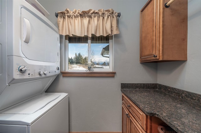 clothes washing area featuring cabinet space, a textured wall, and stacked washing maching and dryer