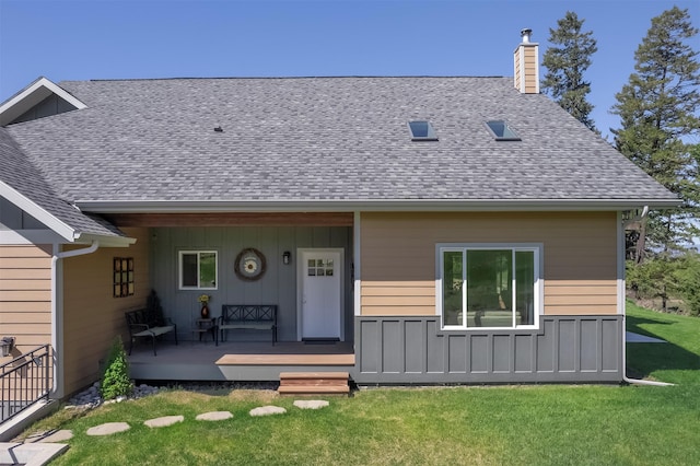 view of front of home with a chimney, a front yard, roof with shingles, board and batten siding, and a wooden deck