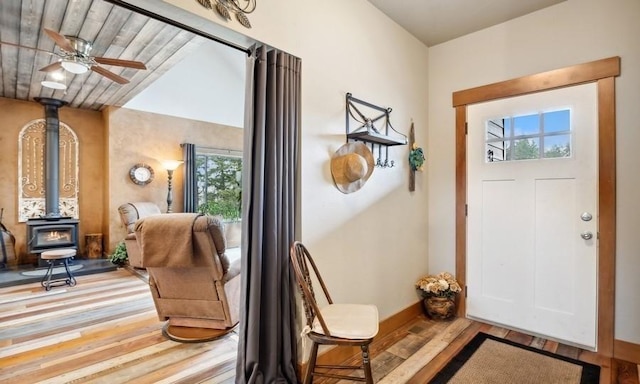 entryway featuring a wood stove, wood finished floors, baseboards, and ceiling fan