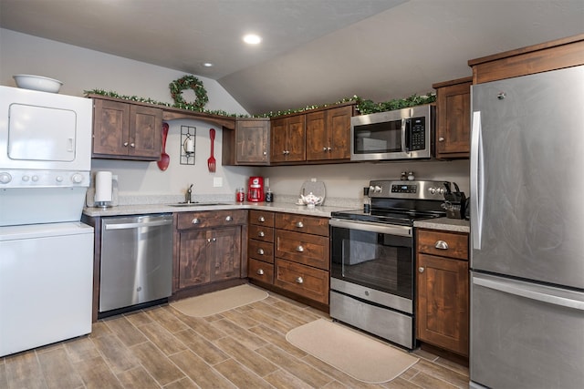 kitchen with stainless steel appliances, stacked washer / dryer, lofted ceiling, a sink, and dark brown cabinets