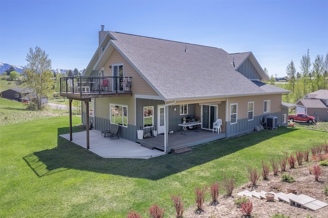back of property featuring central AC, board and batten siding, a balcony, and a lawn