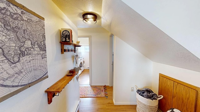 hall with light wood-style flooring, baseboards, vaulted ceiling, and a textured ceiling