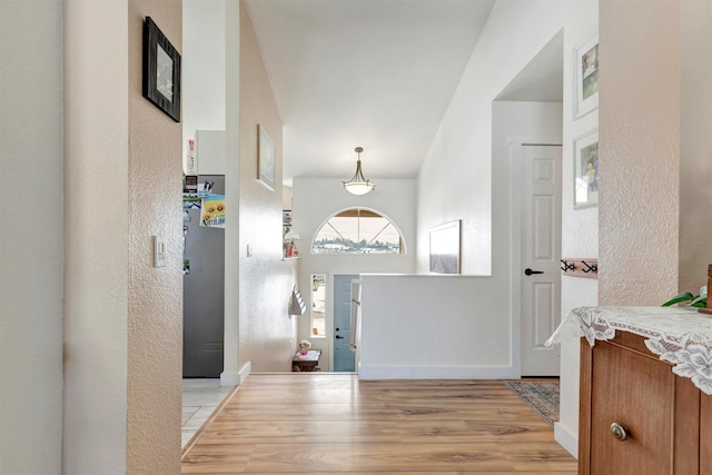 entryway featuring baseboards, a textured wall, and light wood-style floors