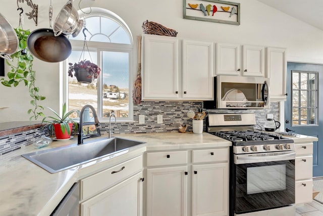 kitchen with lofted ceiling, white cabinetry, stainless steel appliances, and a sink