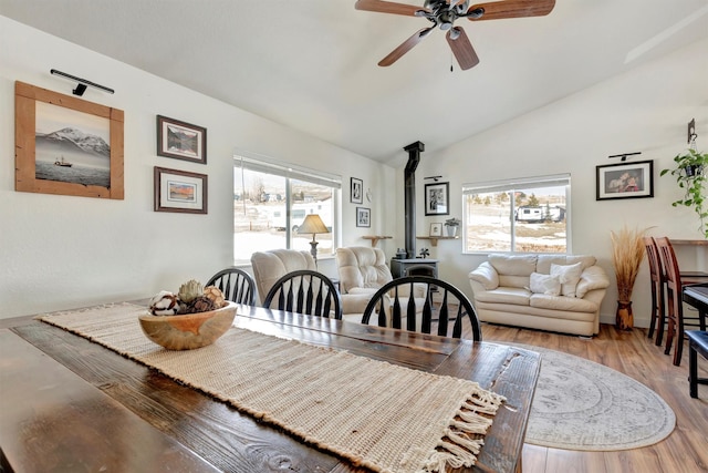 dining space featuring a ceiling fan, lofted ceiling, a wood stove, and wood finished floors