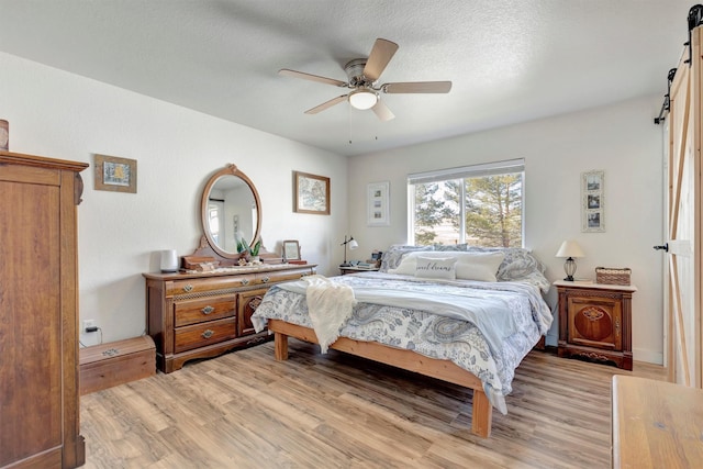 bedroom featuring light wood finished floors, a barn door, a textured ceiling, and a ceiling fan