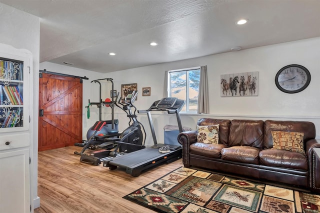 exercise room featuring a barn door, wood finished floors, and recessed lighting