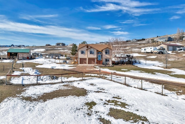 snow covered rear of property featuring a garage, stucco siding, a fenced front yard, and an outdoor structure