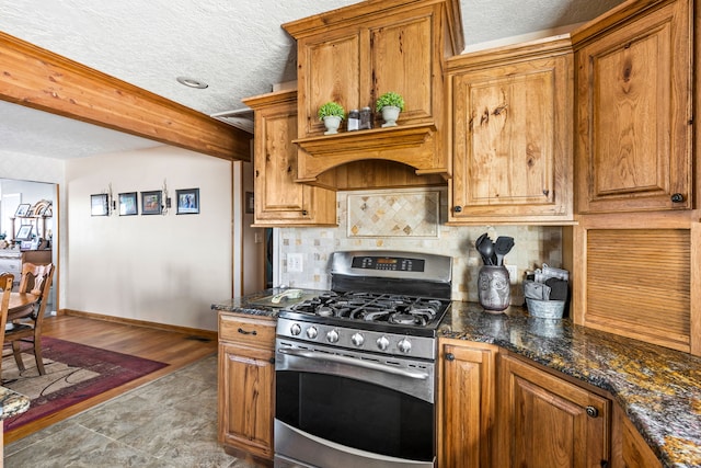 kitchen with tasteful backsplash, brown cabinetry, a textured ceiling, stainless steel gas range oven, and baseboards