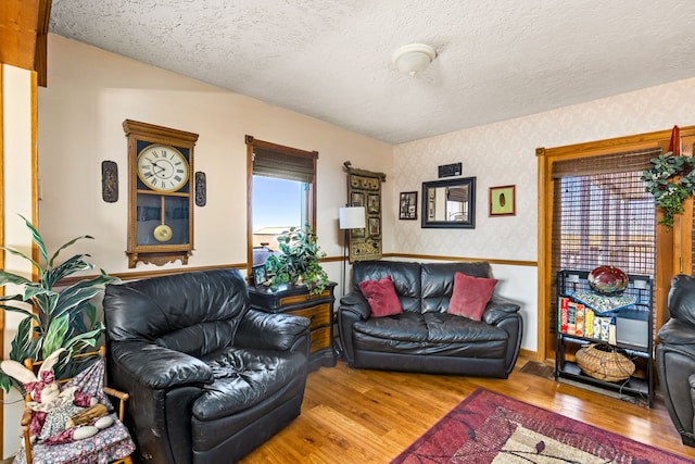 living room with wood finished floors, a textured ceiling, and wallpapered walls