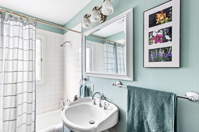 bathroom with a textured wall, plenty of natural light, a sink, and shower / tub combo