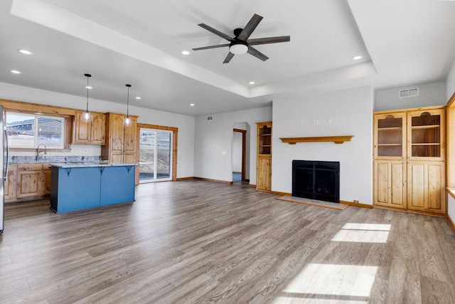 unfurnished living room featuring visible vents, a fireplace with raised hearth, arched walkways, wood finished floors, and a tray ceiling