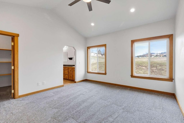 unfurnished bedroom featuring lofted ceiling, arched walkways, connected bathroom, light carpet, and baseboards