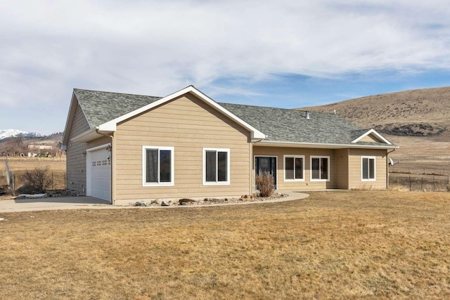 view of front of home with a garage, a shingled roof, fence, a mountain view, and a front yard