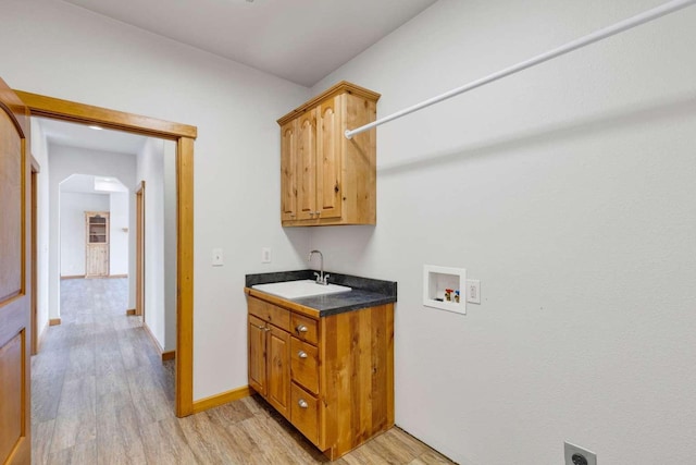 laundry area with hookup for a washing machine, a sink, baseboards, light wood-type flooring, and cabinet space