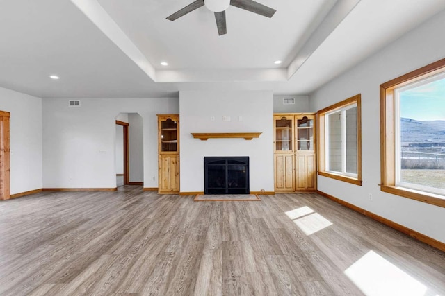 unfurnished living room with light wood finished floors, a raised ceiling, visible vents, and baseboards