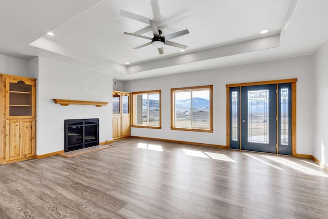 unfurnished living room with a fireplace with flush hearth, wood finished floors, a ceiling fan, baseboards, and a raised ceiling