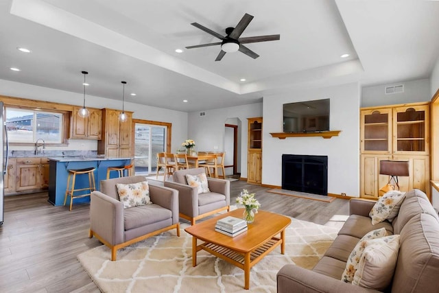 living room with recessed lighting, a raised ceiling, visible vents, and light wood-style flooring