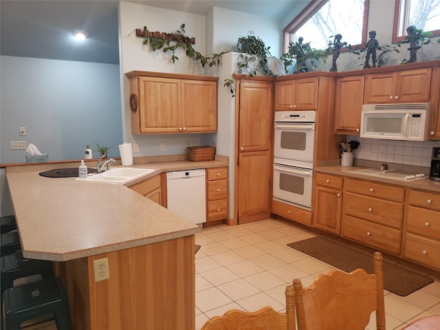 kitchen with white appliances, a peninsula, light countertops, a sink, and light tile patterned flooring