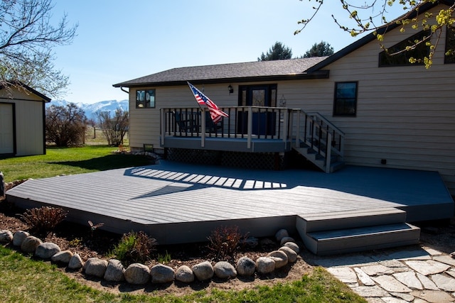 back of property with an outdoor structure, a deck with mountain view, a yard, a shingled roof, and a storage shed