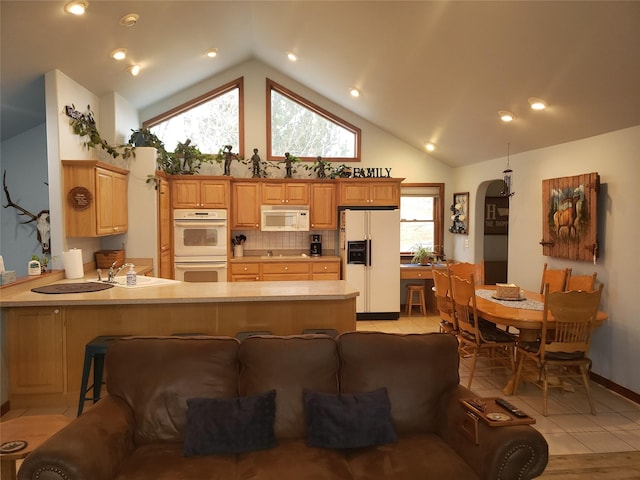 kitchen with arched walkways, a peninsula, white appliances, light countertops, and backsplash