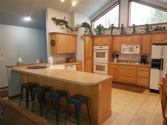 kitchen with a breakfast bar area, light countertops, light tile patterned flooring, a sink, and white appliances