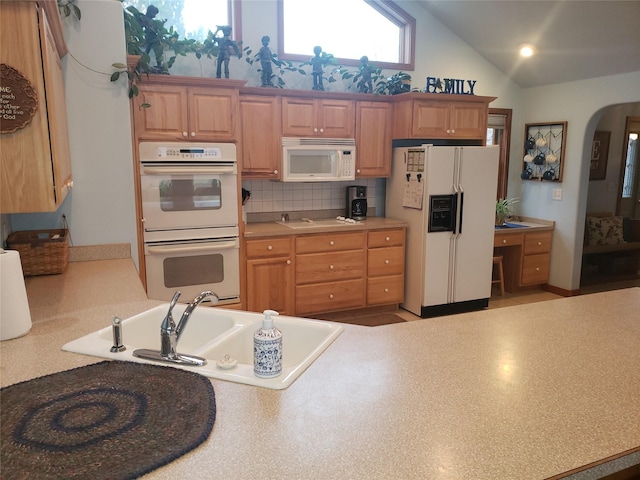 kitchen featuring arched walkways, light countertops, backsplash, a sink, and white appliances