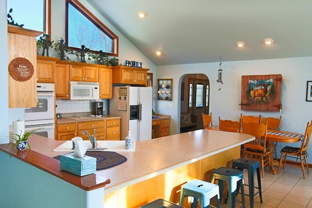 kitchen with decorative backsplash, light tile patterned floors, a kitchen bar, white appliances, and arched walkways