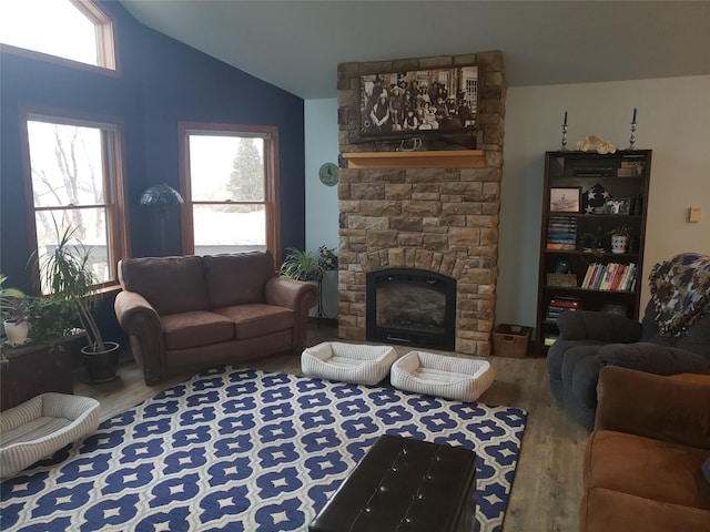 living room with plenty of natural light, vaulted ceiling, wood finished floors, and a stone fireplace