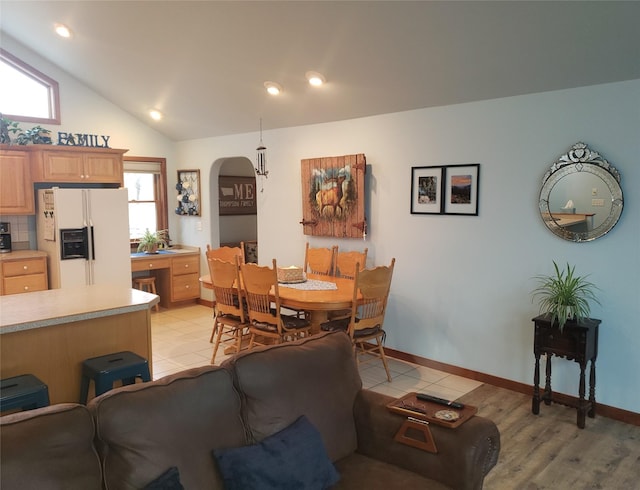 dining area with light tile patterned floors, baseboards, arched walkways, and vaulted ceiling