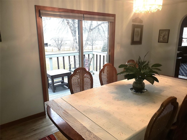 dining space with baseboards, arched walkways, a notable chandelier, and wood finished floors