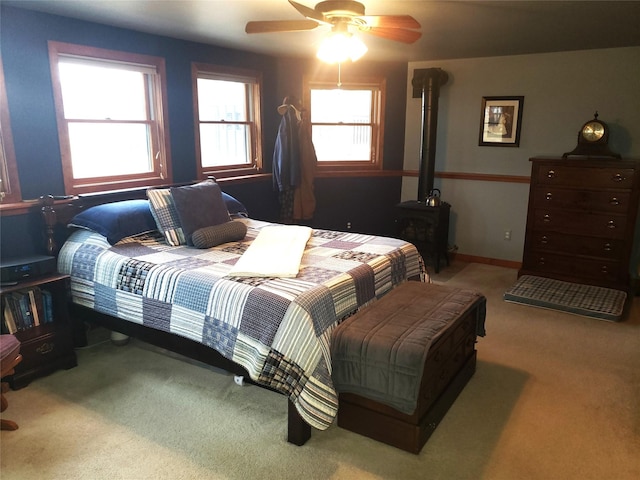 carpeted bedroom with a wood stove, ceiling fan, multiple windows, and baseboards