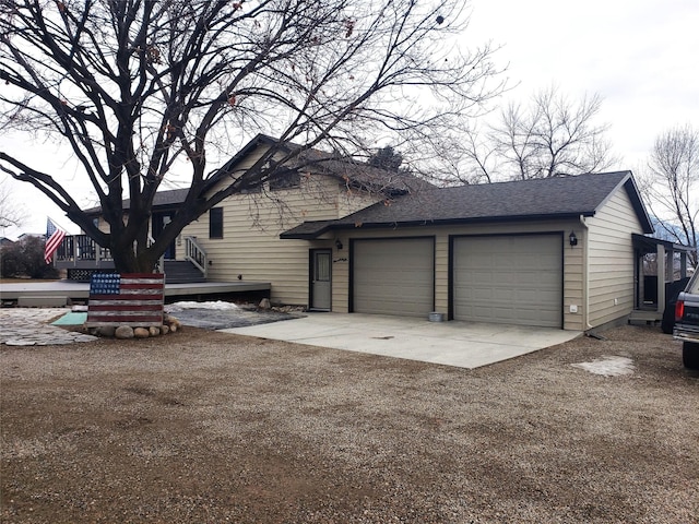 view of side of property featuring driveway, roof with shingles, an attached garage, and a wooden deck