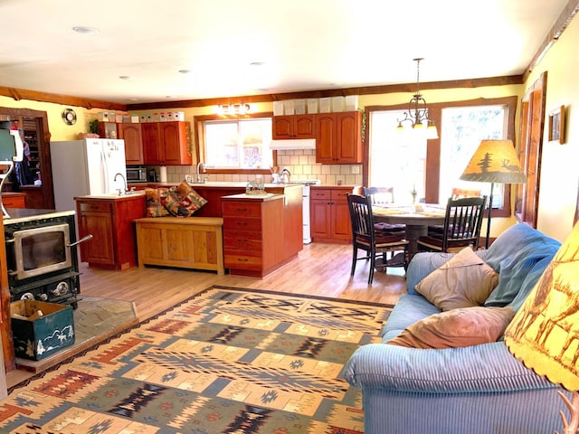 kitchen with open floor plan, light wood-type flooring, decorative backsplash, stainless steel microwave, and pendant lighting