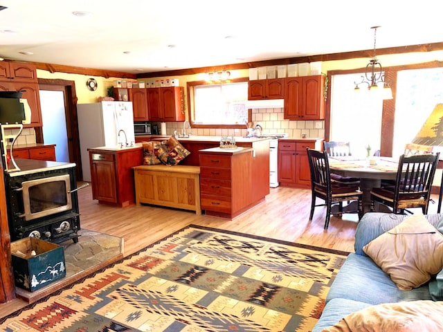 kitchen with black microwave, a wood stove, light wood-style floors, backsplash, and a center island with sink