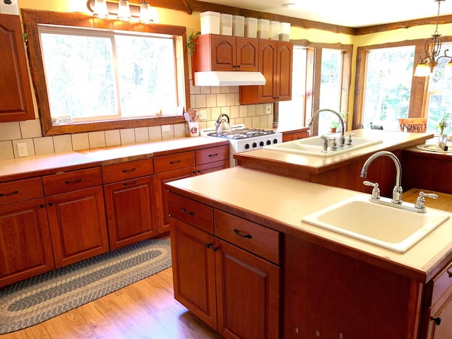 kitchen featuring light wood-style floors, a sink, under cabinet range hood, and an inviting chandelier