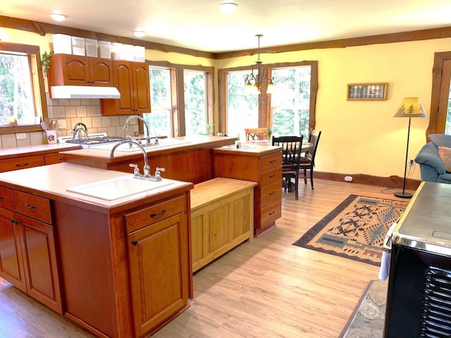 kitchen with a wealth of natural light, light countertops, backsplash, light wood-style floors, and under cabinet range hood