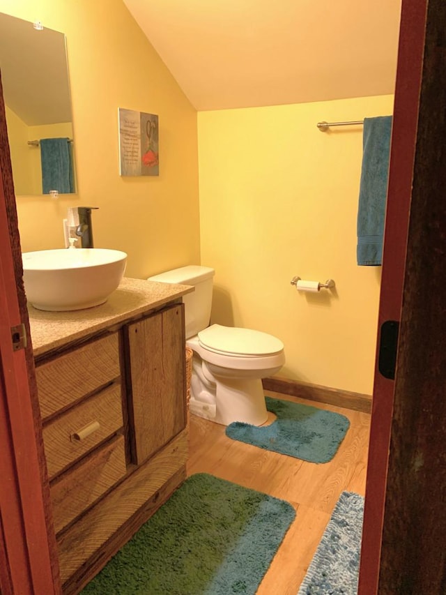 half bathroom featuring lofted ceiling, toilet, wood finished floors, vanity, and baseboards