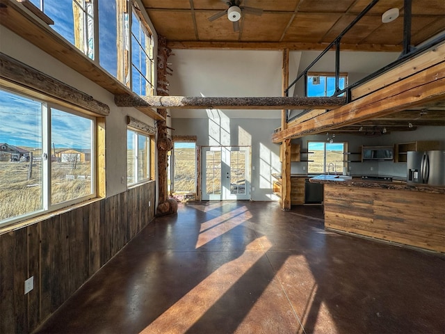 living area with concrete flooring, wood walls, a towering ceiling, and ceiling fan