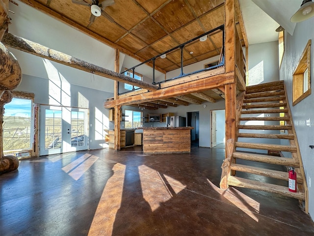 unfurnished living room featuring concrete floors, a healthy amount of sunlight, a high ceiling, and stairway