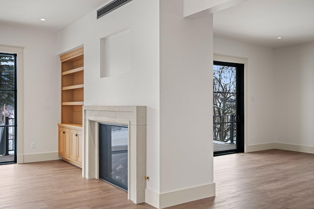 unfurnished living room with recessed lighting, light wood-type flooring, a glass covered fireplace, and baseboards