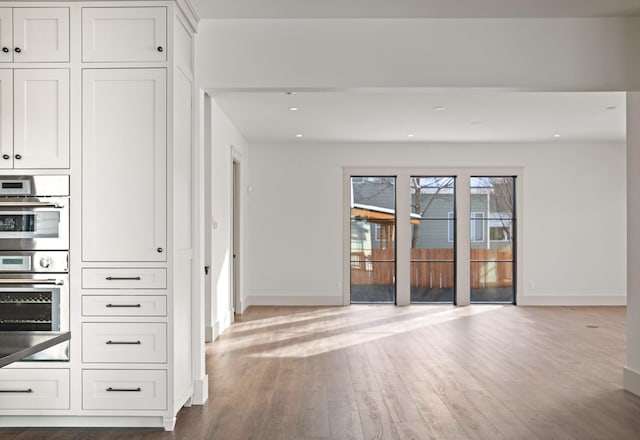 interior space with open floor plan, stainless steel double oven, wood finished floors, and baseboards