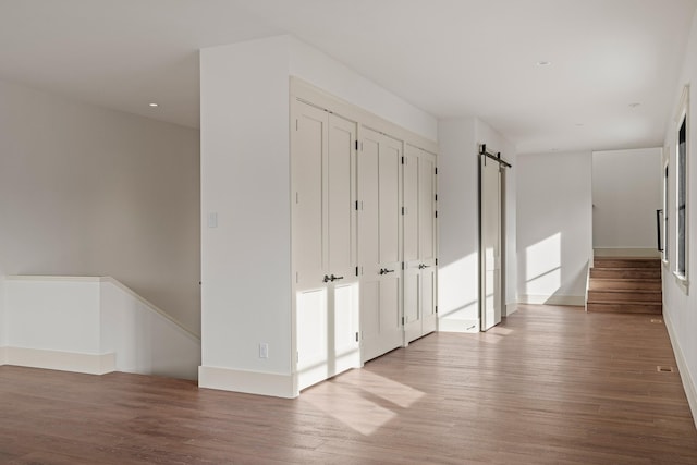 unfurnished room featuring a barn door, wood finished floors, and baseboards