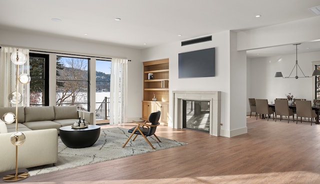 living area featuring built in shelves, recessed lighting, visible vents, a glass covered fireplace, and wood finished floors