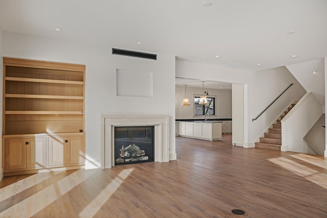 unfurnished living room with visible vents, a glass covered fireplace, stairway, wood finished floors, and recessed lighting